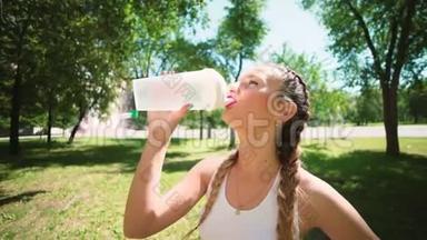 苗条的年轻女人在训练后喝水。 女运动员休息，她喝水，在炎热的跑步<strong>中外</strong>出